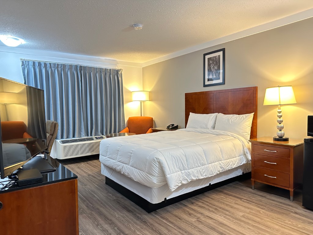 King bed guest room with white bedding, wood headboard, and sitting area at Sunset Inn and Suites in Sioux Lookout